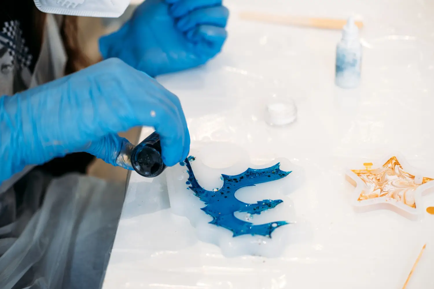 Person in blue gloves making resin crafts, blue leaf shape and gold star.