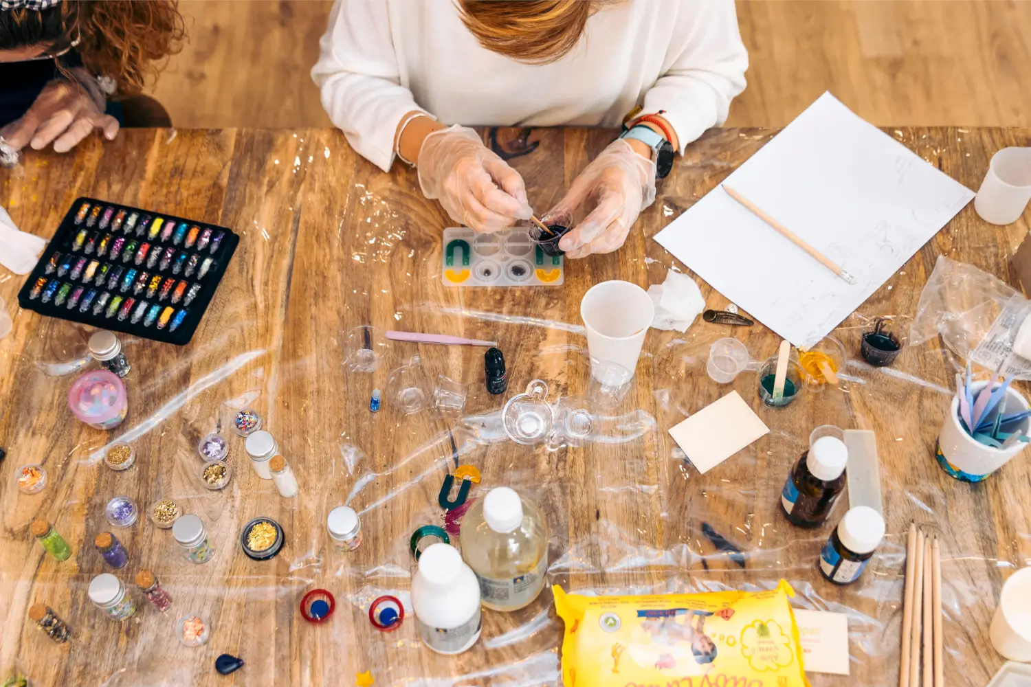 Overhead view of craft supplies for resin art project. Glitter, dyes, molds, and tools on a wooden table.