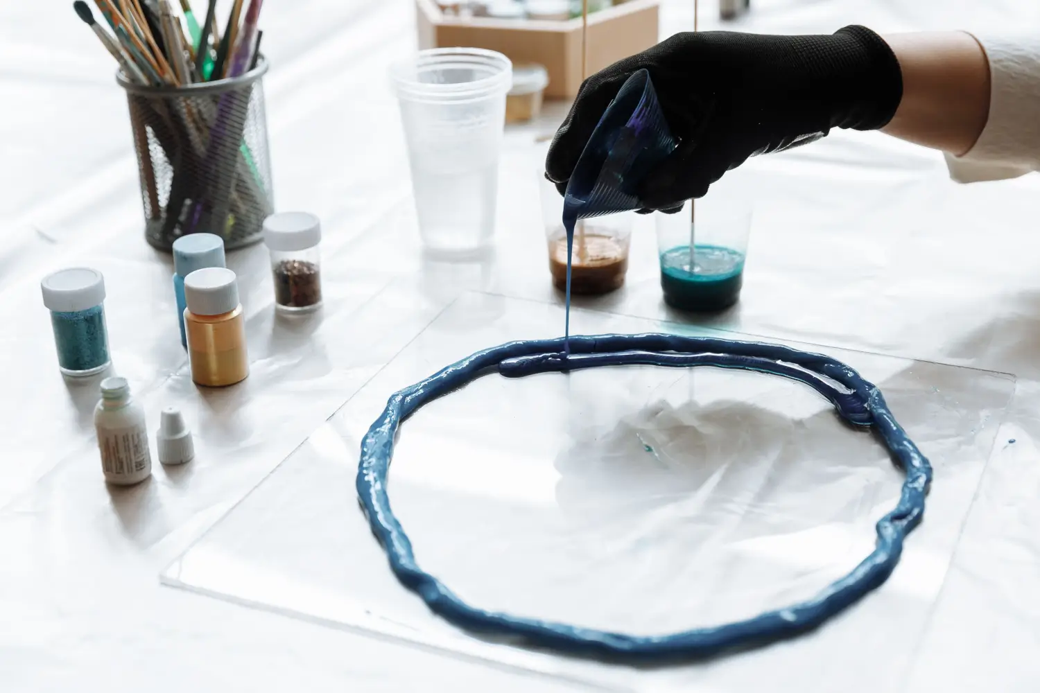 Person pouring blue resin into a circle on a table.  Crafting supplies.