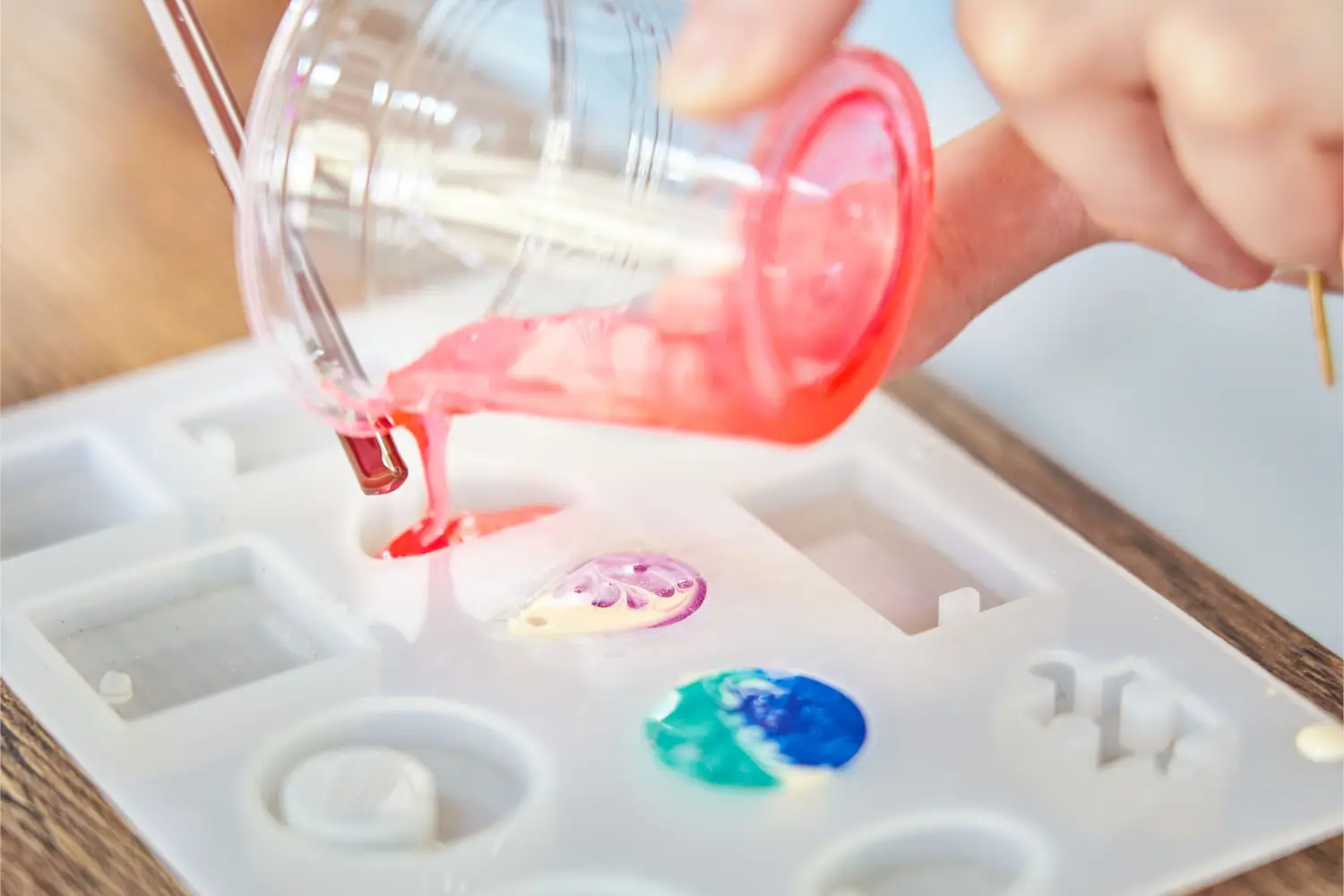 Person pouring resin into silicone mold for jewelry making.