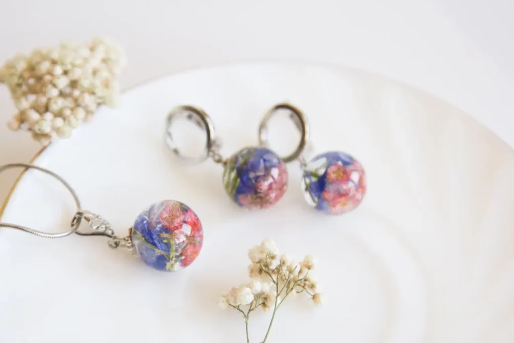 Floral resin earrings and necklace, pink and blue flowers, silver metal, on white plate.