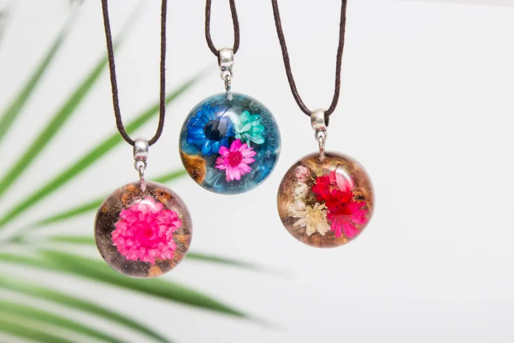 Three round pendants, each with preserved flowers encased in resin, on brown cords.  Blue, pink, and red flowers.