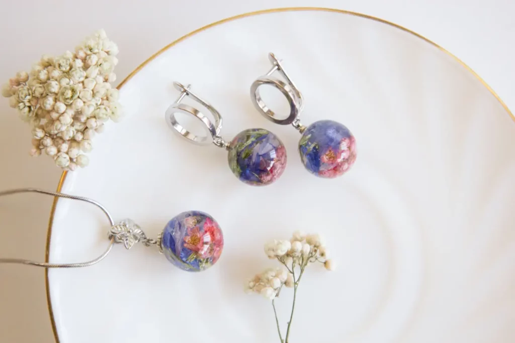 Silver-toned earrings and necklace with pressed flowers in resin, on a white plate.