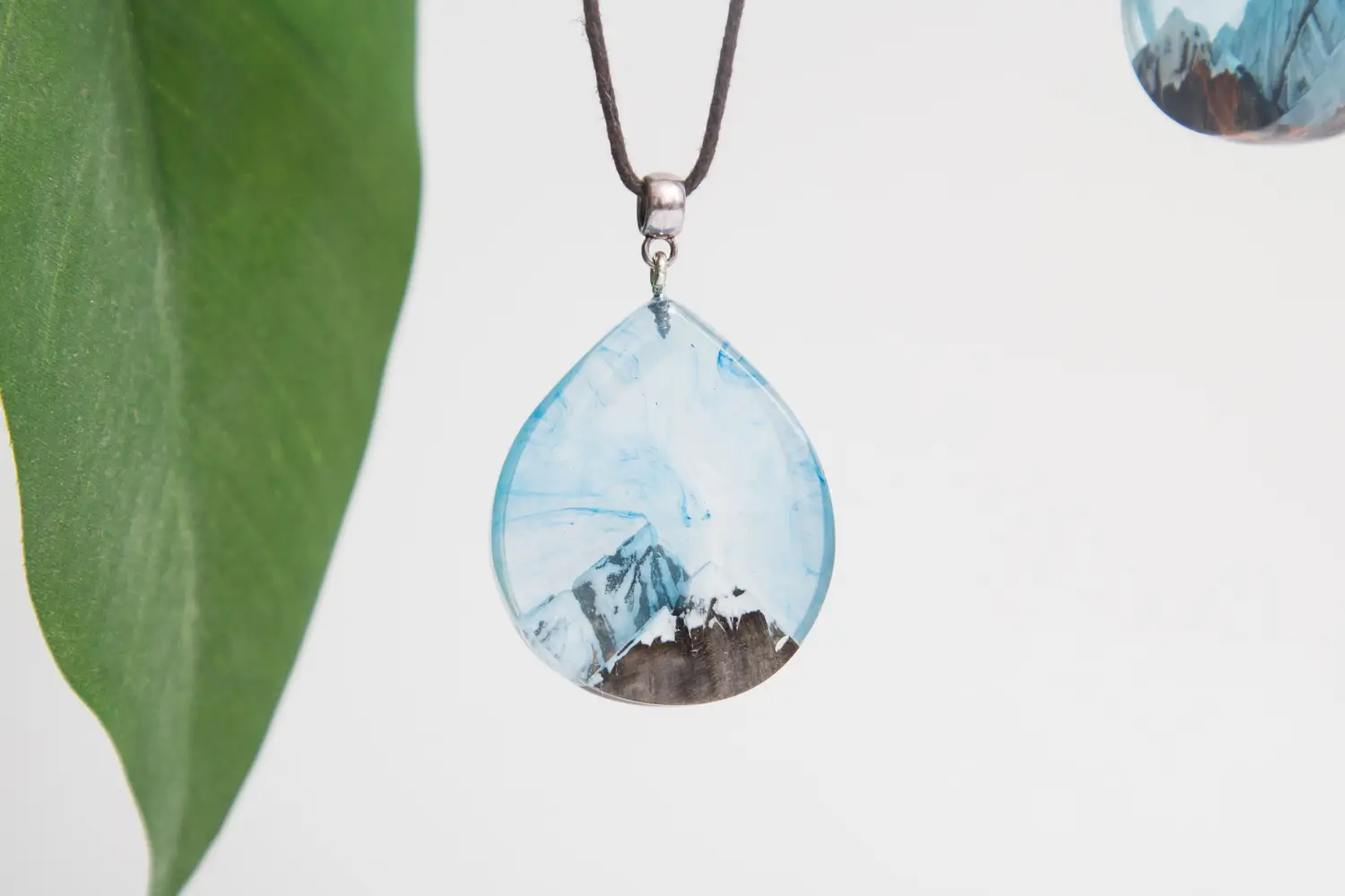 Light-blue resin pendant, mountains scene, dark wood inlay.